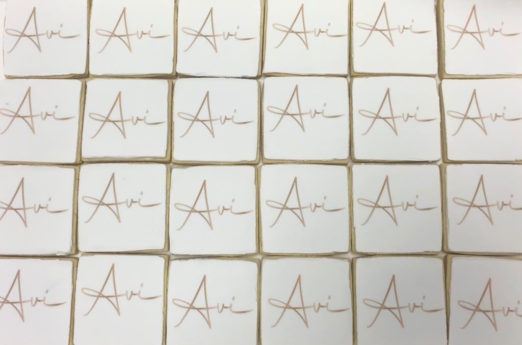 White square cookies with a name piped in rose-gold script